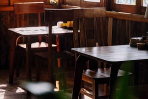 A rustic wooden interior with tables and chairs, wooden beams on the ceiling, and a window allowing natural light. - The Hill Sapa (TT. Sa Pa)