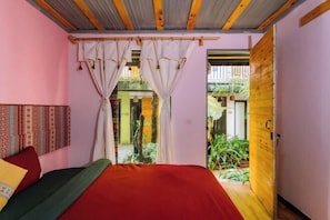 Un dormitorio con cama, cortinas, una puerta de madera y vistas a un espacio exterior.