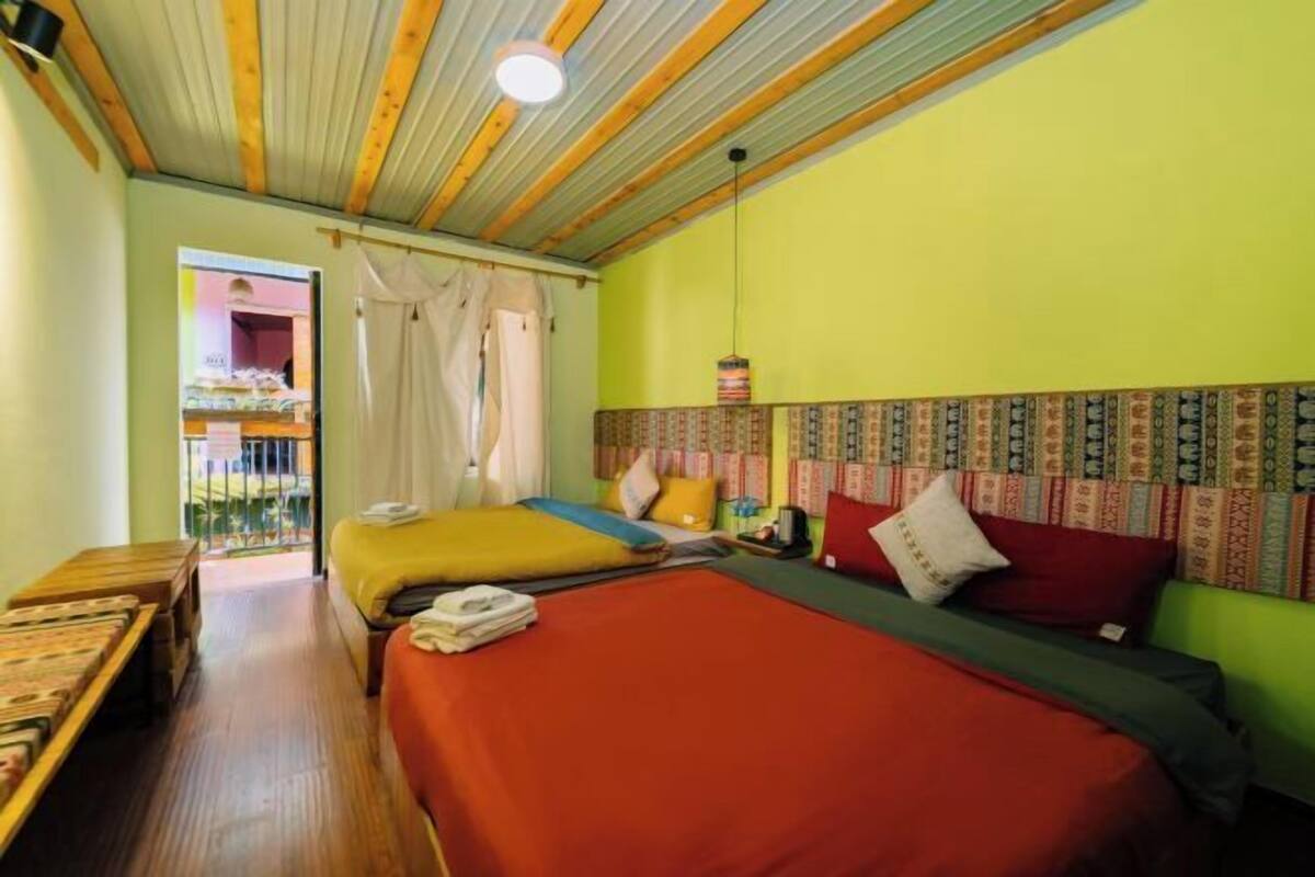 A room with two beds, a wooden bench, a ceiling with wooden beams, and a patterned headboard.