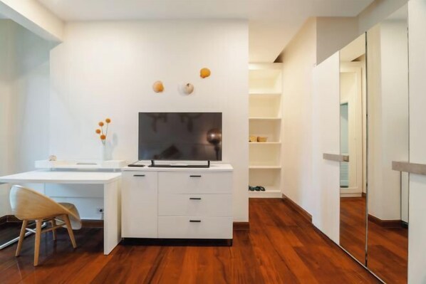 Una habitación moderna con un escritorio blanco, televisor y espejo.