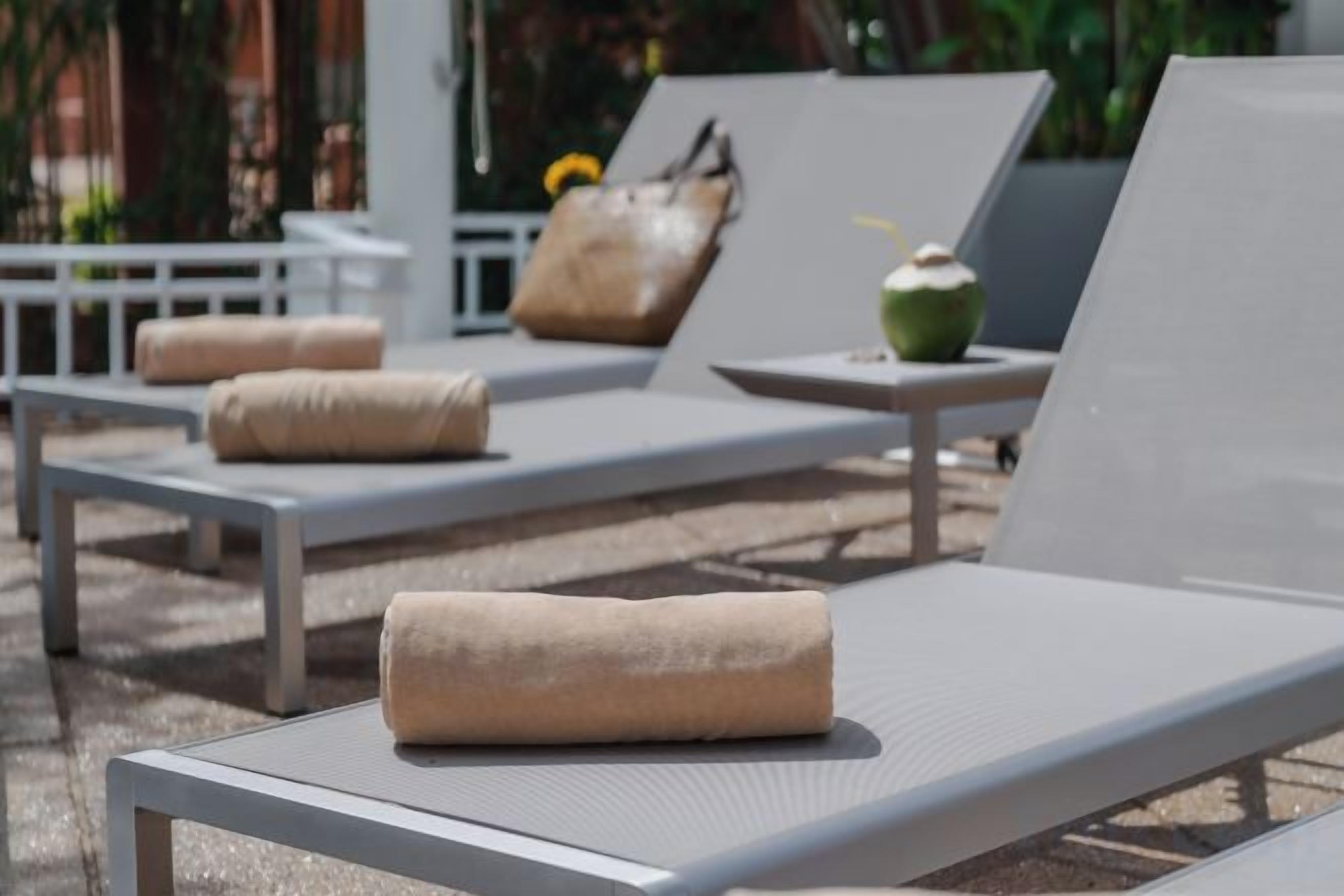 A row of sun loungers with towels, a coconut drink, and a white chair.