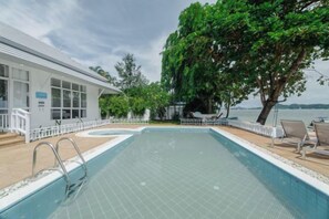 Una piscina con vistas al mar, un edificio blanco y un árbol grande.