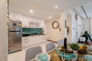 A compact kitchen with white cabinets, a stainless steel refrigerator, and a green tiled backsplash. - Seaside Bliss Villa Rawai (Phuket)