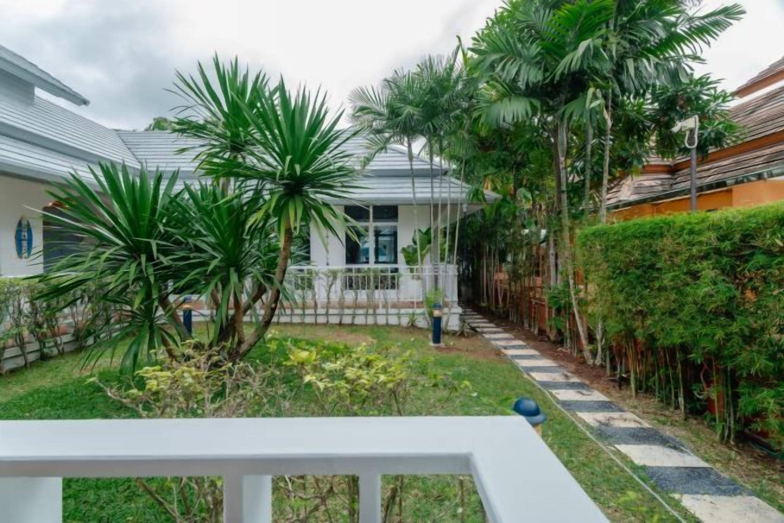 Een binnenplaats met een witte balustrade, palmbomen en een pad naar een gebouw.