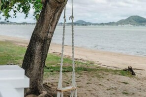 A beach scene with a swing hanging from a tree, a sandy shore, and a body of water in the background. - Seaside Bliss Villa Rawai (Phuket)