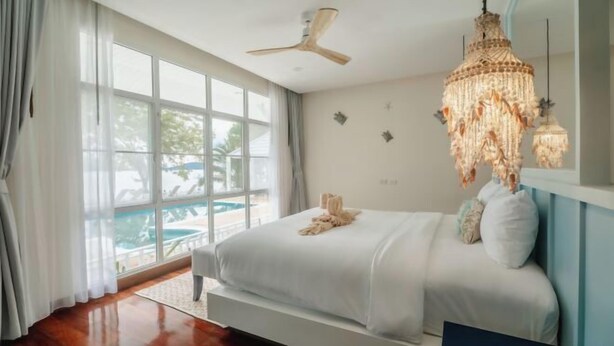 A bedroom with a large bed, a ceiling fan, a chandelier, and a view of a pool. - Seaside Bliss Villa Rawai (Phuket)