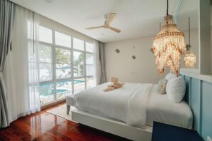 Un dormitorio con una cama grande, ventilador de techo, candelabro y vista a una piscina.