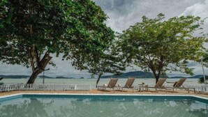 A swimming pool with lounge chairs and a white fence, surrounded by trees and a view of the sea. - Seaside Bliss Villa Rawai (Phuket)