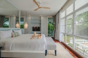 Een slaapkamer met een groot bed, een plafondventilator, een televisie en een balkon met uitzicht op groen.