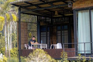 A man sitting at a table on an outdoor balcony with a view of tropical vegetation. - Cheiwlan Camp & Resort (Ban Ta Khun)
