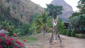 A rustic wooden swing set in a natural setting with a mountain in the background.