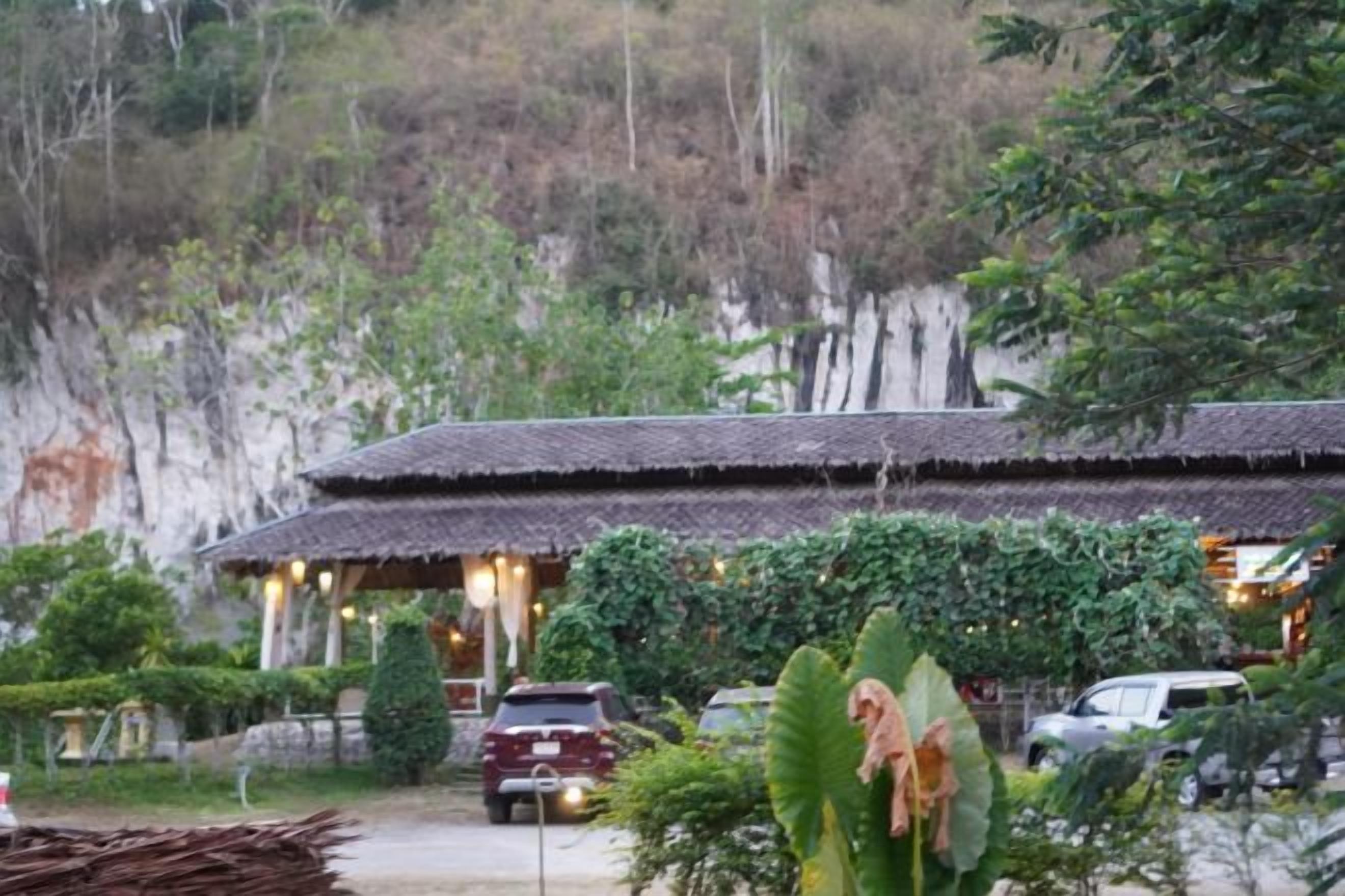 A traditional building with a thatched roof, surrounded by greenery and a rocky hillside.