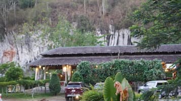 A traditional building with a thatched roof, surrounded by greenery and a rocky hillside.