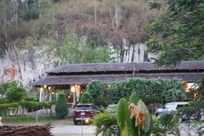 A traditional building with a thatched roof, surrounded by greenery and a rocky hillside. - Cheiwlan Camp & Resort (Ban Ta Khun)