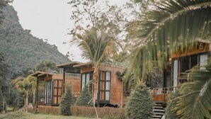 Un bâtiment moderne à l’extérieur en bois, entouré d’une végétation luxuriante et adossé à un paysage montagneux.