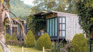 Une cabane en bois dotée de grandes fenêtres, entourée de jardins bien entretenus et avec une chaîne de montagnes en toile de fond.