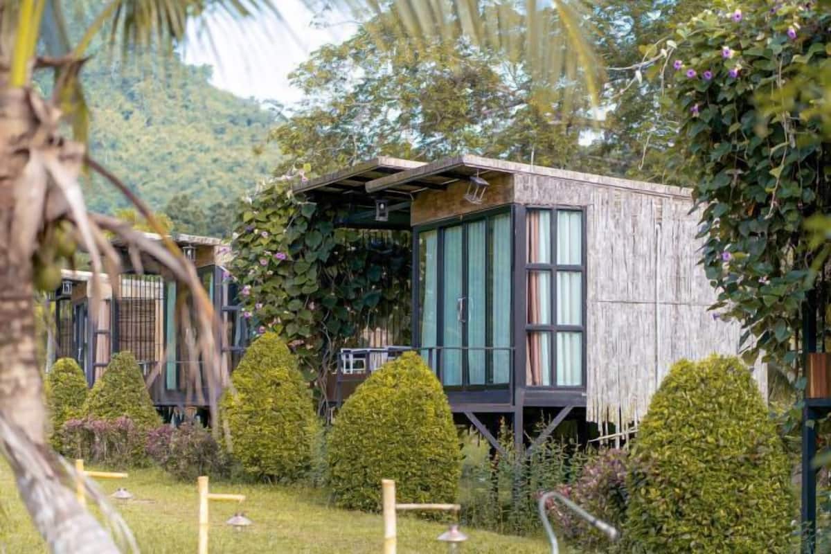 Eine Holzhütte mit großen Fenstern, umgeben von gepflegten Gärten und einer Bergkulisse.