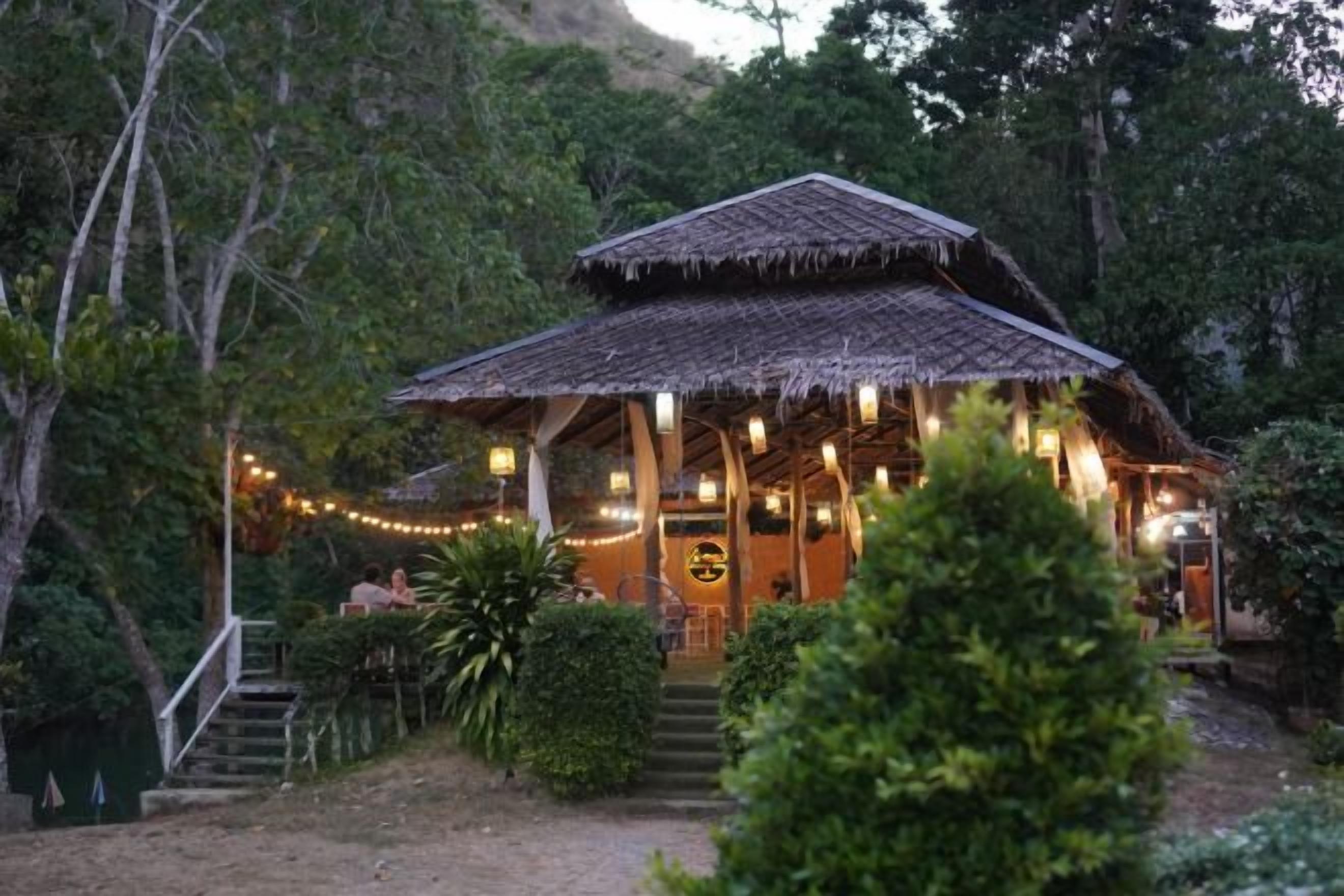 A rustic thatched-roof building with a porch, surrounded by greenery.