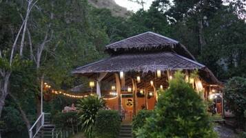 A rustic thatched-roof building with a porch, surrounded by greenery.