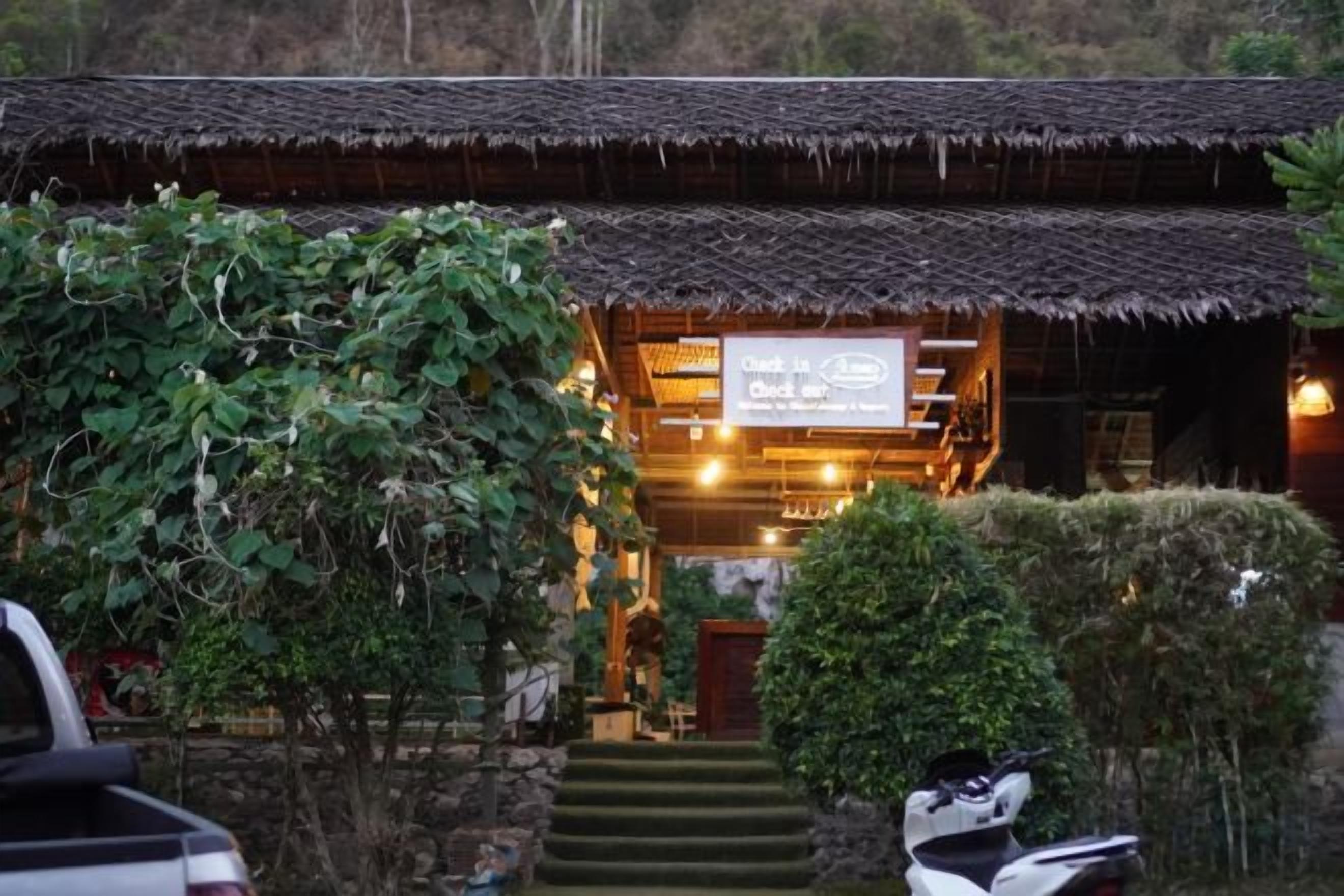 A traditional building with a thatched roof, a visible staircase leading to the entrance, and a signboard with text.