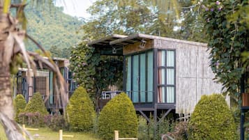 Una cabaña de madera con balcón, rodeada de exuberante vegetación y un telón de fondo montañoso.