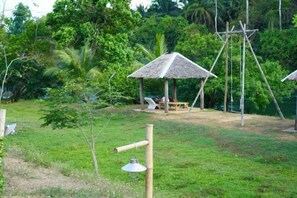 A grassy area with a thatched-roof structure, a swing set, and a small table with chairs. - Cheiwlan Camp & Resort (Ban Ta Khun)