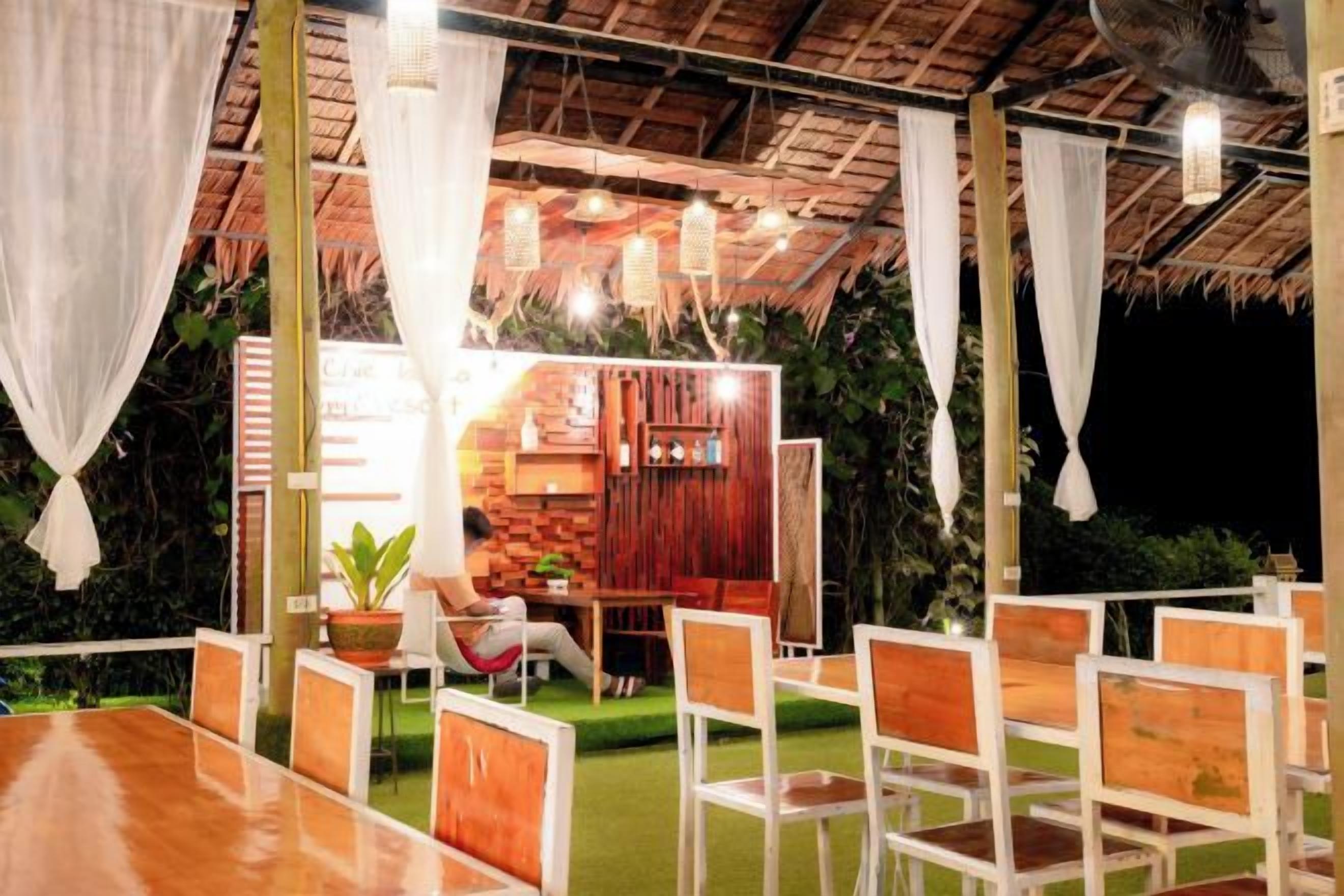 An outdoor dining area with wooden tables and chairs, a brick wall, and hanging lights.