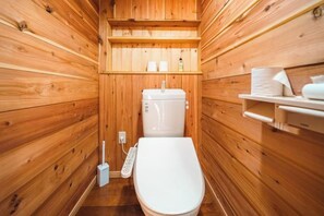 A small, wooden-paneled bathroom with a toilet, a shelf with toiletries, and a mop. - Pukōji Temple (Numata)