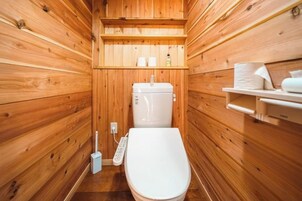 Un baño pequeño con paneles de madera, un inodoro, un estante con artículos de aseo y un trapeador.