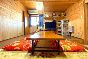A wooden interior with a dining table, pillows, a small dog, and a TV. - Pukōji Temple (Numata)