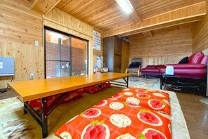 A wooden interior with a long table, a bed with a red floral bedspread, and a red sofa. - Pukōji Temple (Numata)