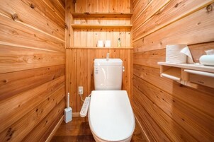 Un baño tipo cabaña de madera con inodoro, estante con artículos de aseo y piso de madera.