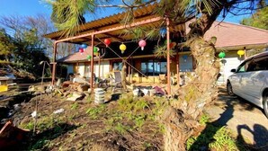 A house with a covered porch, a car parked in front, and a tree with hanging decorations. - Pukōji Temple (Numata)
