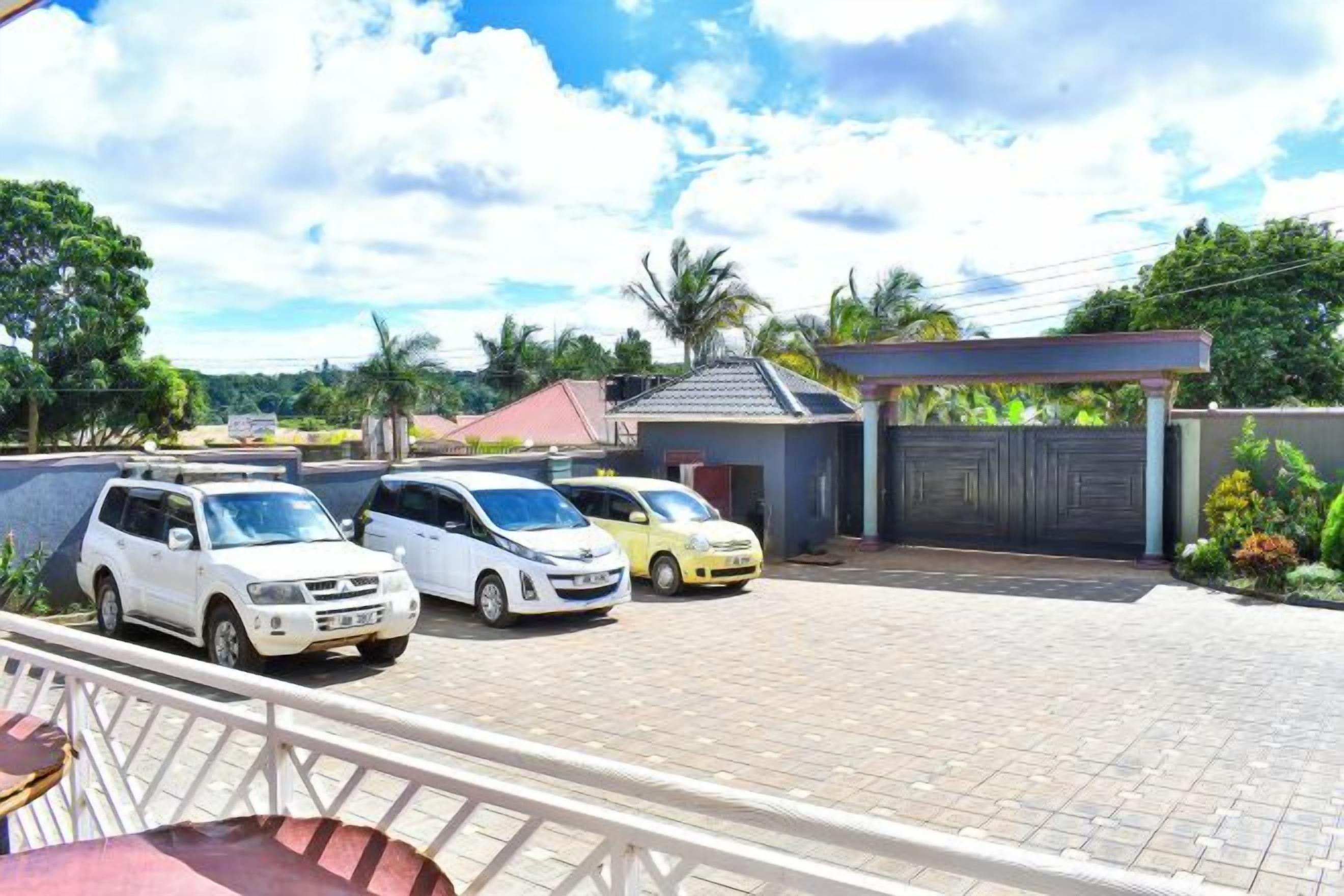 A parking area with several cars, a gated entrance, and a building with a sloped roof.