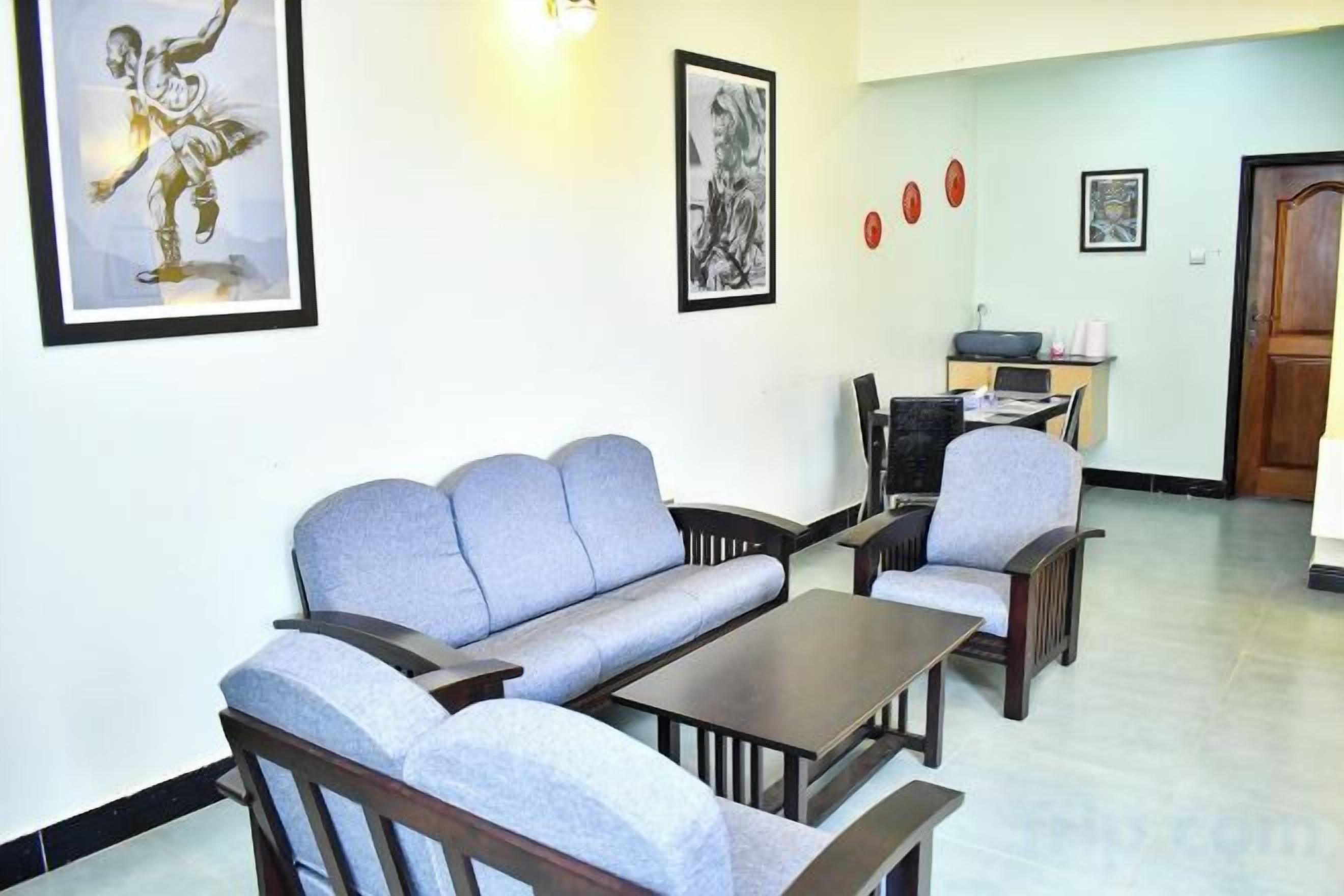 Un salon avec un canapé, des fauteuils et une table basse. Des tableaux encadrés ornent le mur.