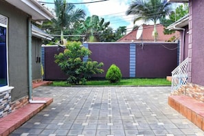 A paved courtyard with a purple wall, a small tree, and a white railing. - The Biira Residence (Busiro)