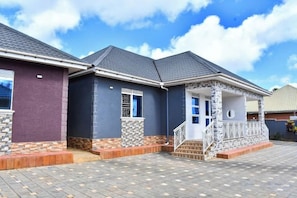 A residential building with a covered porch, a brick pathway, and a clear sky. - The Biira Residence (Busiro)