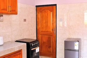 A kitchen with a wooden door, a stove, and a refrigerator. - The Biira Residence (Busiro)