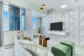 Una sala de estar moderna con un sofá, un reposapiés y un televisor de pantalla plana montado en la pared.