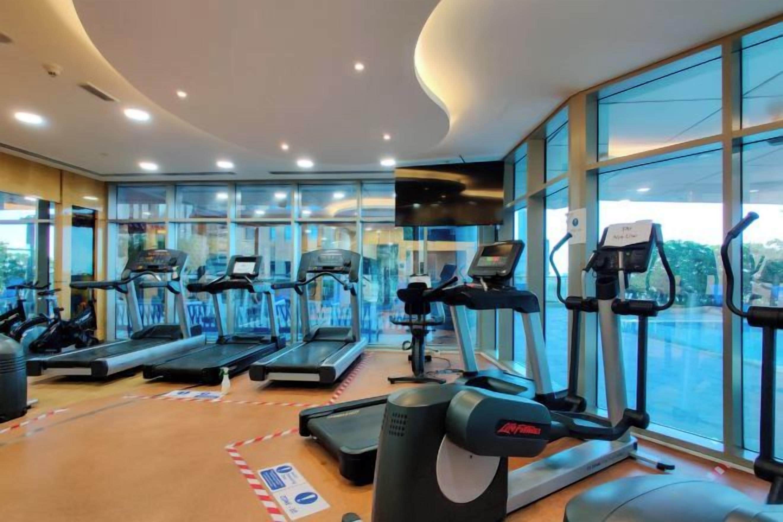 Une salle de sport équipée de tapis de course, de vélos d’appartement et d’autres appareils d’exercice.