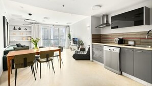 A modern kitchen with a dishwasher, a dining area with a table and chairs, and a living area with a sofa and a TV. - Magnificent Seaside Panorama Stay by Sea N' Rent (Tel Aviv)