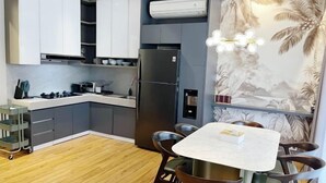 A modern kitchen with grey cabinets, a black refrigerator, a dining table with chairs, and a wall-mounted air conditioner. - Premium Luxury Home At Golf Island PIK (North Jakarta)