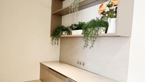 A kitchen with a white countertop, hanging plants, and a white vase with flowers. - Premium Luxury Home At Golf Island PIK (North Jakarta)
