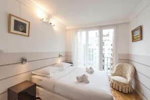 Habitación de hotel con una cama grande, una mesita de noche, una silla y vista a la ciudad por la ventana.