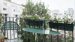 A balcony with a green metal chair and table, potted plants, and a cityscape view.