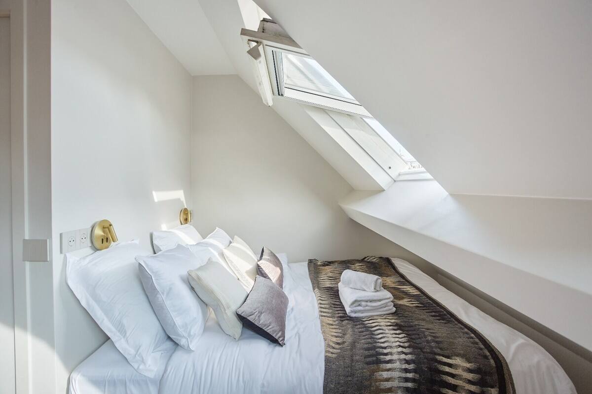 A bedroom with a skylight, a bed with white linens, and a patterned rug.