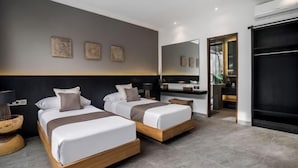 Une chambre d’hôtel moderne avec deux lits, un grand miroir, une armoire sombre et un petit coin salon.
