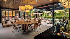 Un intérieur moderne avec une table à manger en bois, des sièges confortables et de grandes fenêtres donnant sur un paysage verdoyant.