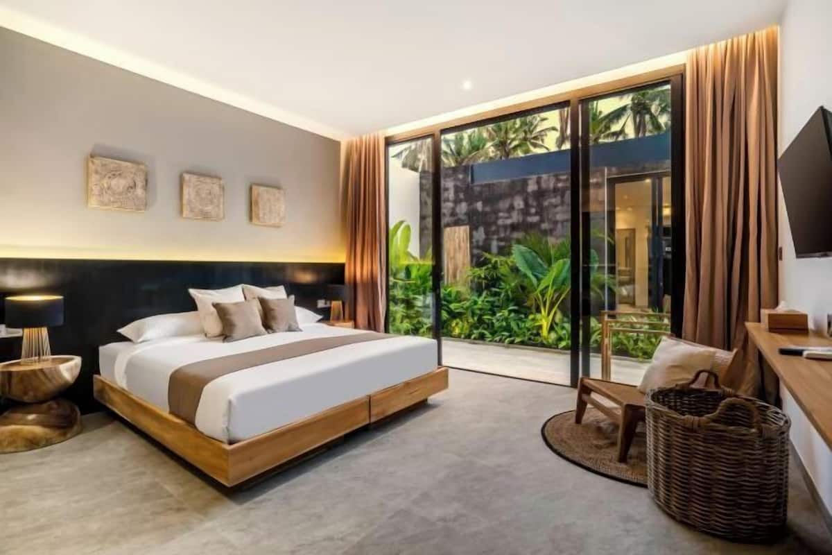 Une chambre moderne avec un grand lit, une télévision et une vue sur la verdure grâce à la porte vitrée.