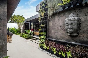 A modern building with a Buddha head sculpture, a concrete wall, and a variety of plants. - Villa Jungle Paradise by BaliSuperHost (Bali)